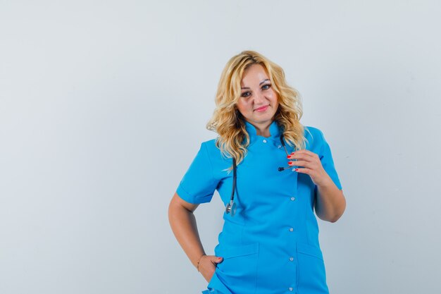 Female doctor looking at camera with hand in pocket in blue uniform and looking contented , space for text