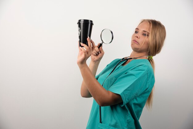 Female doctor looking at cup with magnifying glass.