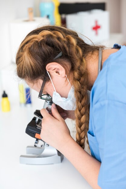 Женский врач, глядя через микроскоп в лаборатории