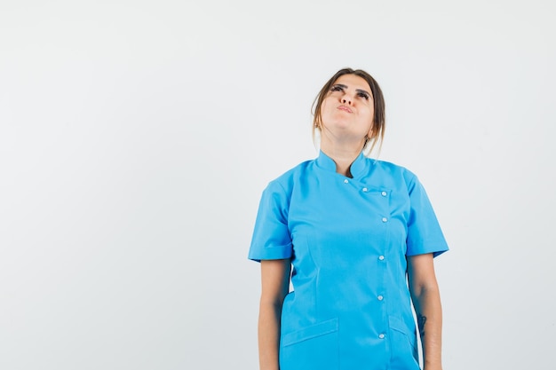 Женщина-врач смотрит вверх в синей форме и смотрит с надеждой