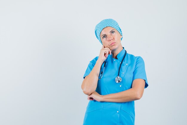 Female doctor looking up in blue uniform and looking pensive. front view.