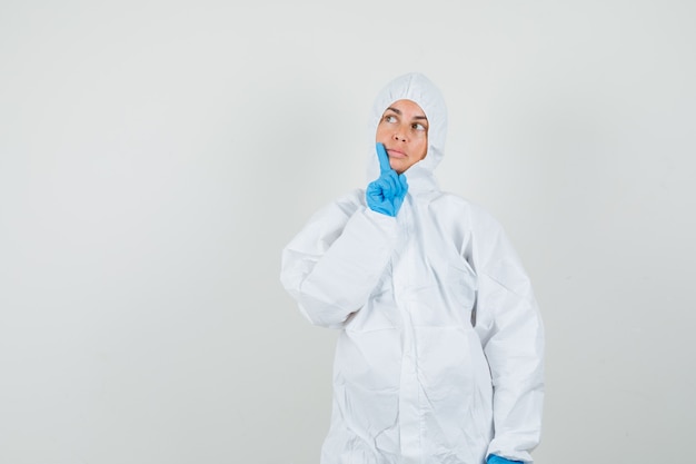 Female doctor looking up in protection suit, gloves and looking indecisive.