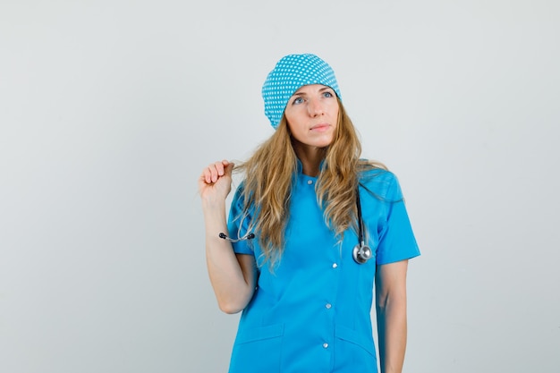 Free photo female doctor looking up while holding strand in blue uniform and looking dreamy