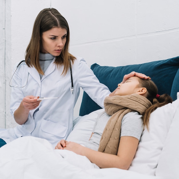 Female doctor measuring temperature of her sick patient lying on bed