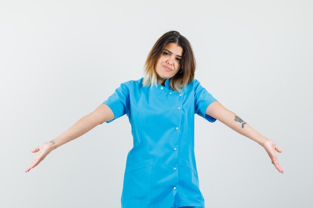Женщина-врач широко раскрывает руки в синей форме и выглядит независимой
