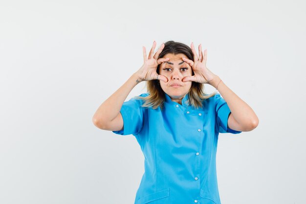 Female doctor opening eyes with fingers in blue uniform and looking tired