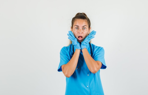 Женщина-врач открывает ладони возле рта в синей форме