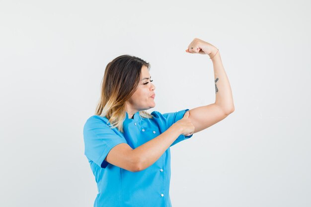 Female doctor pointing at arm muscles in blue uniform and looking powerful