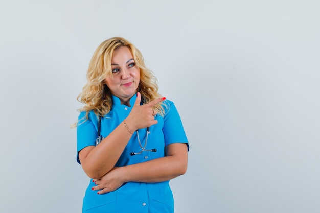 Foto gratuita medico femminile che indica da parte in uniforme blu e che osserva lo spazio concentrato per testo