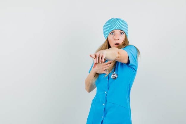 Female doctor pointing away in blue uniform and looking puzzled 