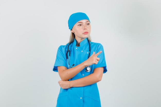 Female doctor pointing away while looking aside in blue uniform 