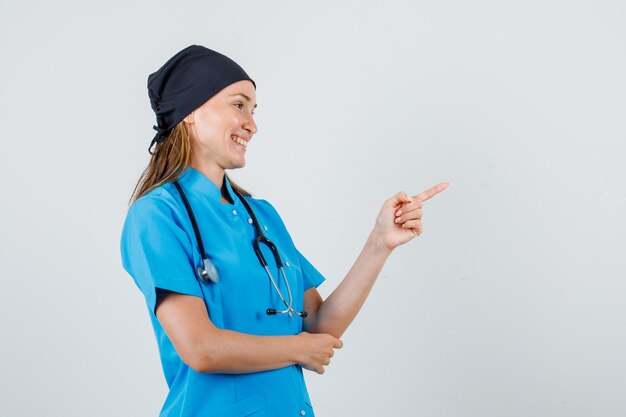 Female doctor pointing finger to side in uniform and looking cheerful. .