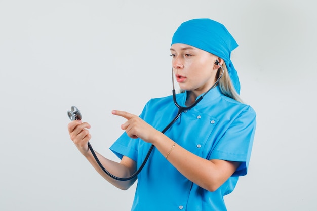 Female doctor pointing finger at stethoscope in blue uniform and looking serious.