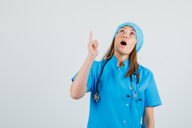 Free photo female doctor pointing finger up in blue uniform and looking focused