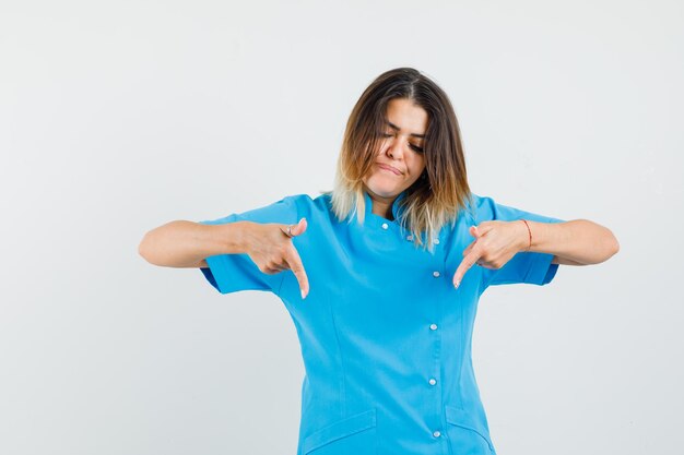 Female doctor pointing fingers down in blue uniform and looking focused