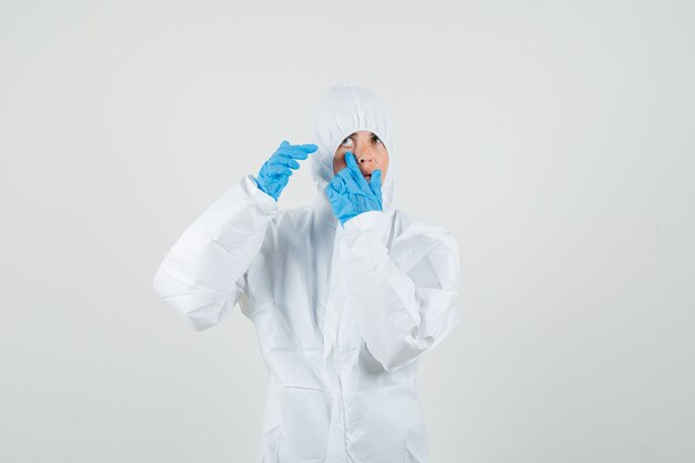 Female doctor pointing at her eyelid pulled by finger in protective suit