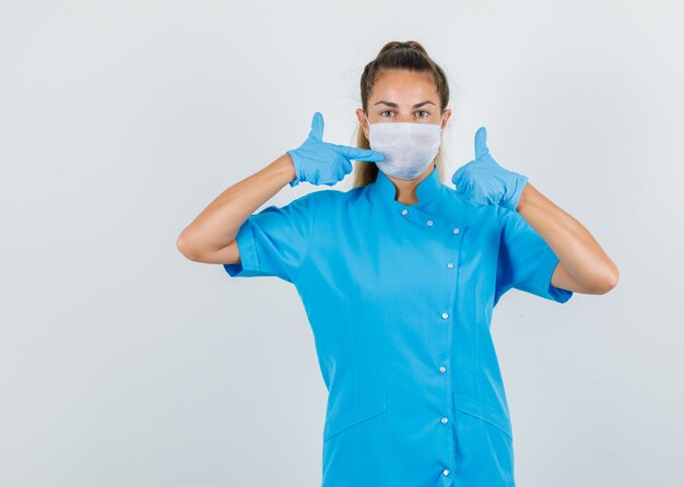 青い制服、手袋、慎重に見て親指でマスクを指している女性医師