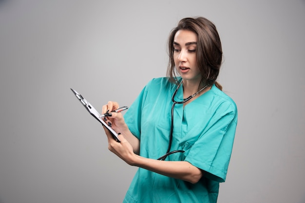 회색 배경에 노트를 가리키는 여성 의사. 고품질 사진