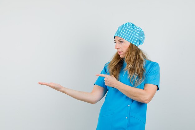 Female doctor pointing at palm spread aside in blue uniform 