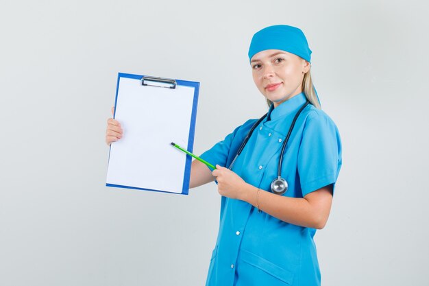 Женщина-врач указывает карандашом на буфер обмена в синей форме и выглядит весело