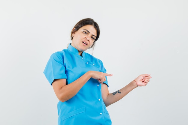파란색 유니폼 측면을 가리키고 자신감을 찾고 여성 의사