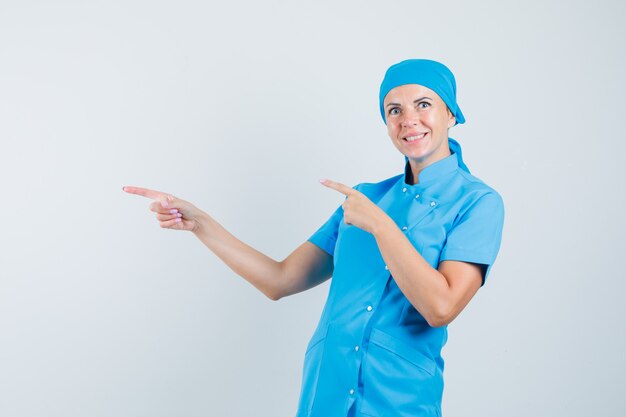 Female doctor pointing to the side in blue uniform and looking merry. front view.