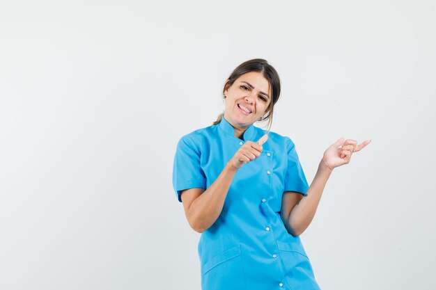 측면을 가리키는 여성 의사, 파란색 유니폼에 엄지 손가락을 표시하고 쾌활한 찾고