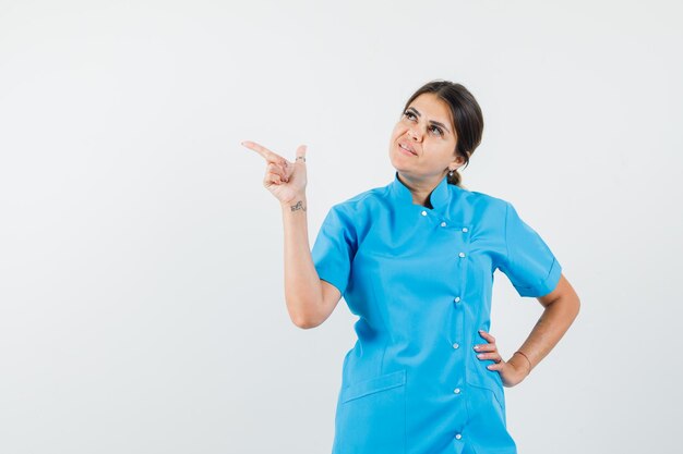 Female doctor pointing to the side while looking up in blue uniform