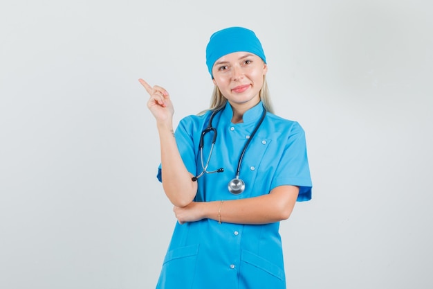 Женщина-врач указывает в сторону пальцем в синей форме и выглядит весело