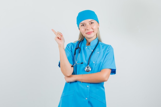 Female doctor pointing to side with finger in blue uniform and looking cheery