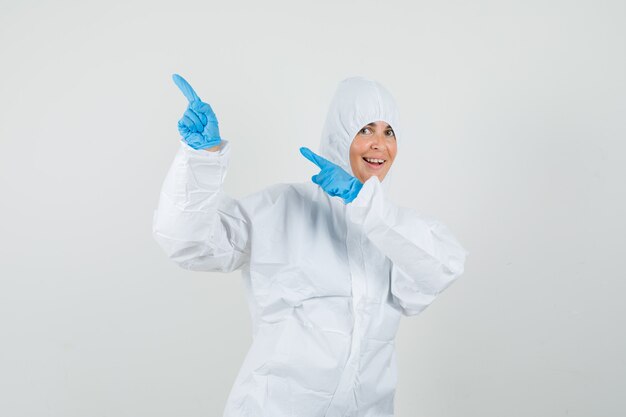 Женщина-врач, указывая в сторону с пальцами вверх в защитном костюме
