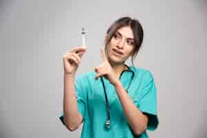 Free photo female doctor pointing at syringe on gray