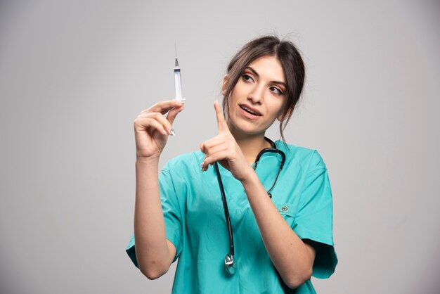 Female doctor pointing at syringe on gray