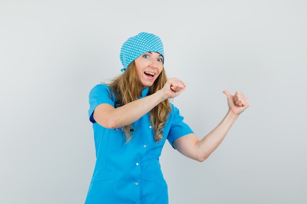 Female doctor pointing thumbs up back in blue uniform and looking curious 