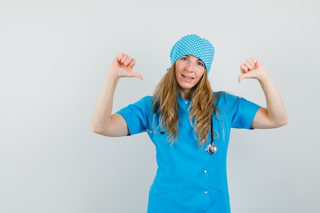 Бесплатное фото Женщина-врач указывает на себя пальцами в синей форме и выглядит уверенно