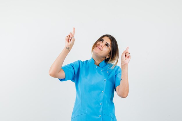 Female doctor pointing up in blue uniform and looking cheerful