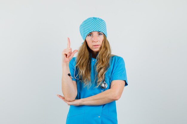 Female doctor pointing up in blue uniform and looking sensible. 