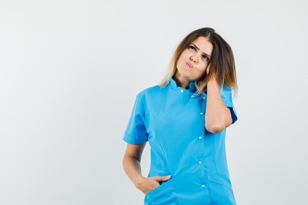 파란색 유니폼을 입고 생각하고 귀여운 찾고있는 동안 포즈를 취하는 여성 의사