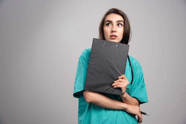 회색 배경에 클립 보드와 함께 포즈를 취하는 여성 의사. 고품질 사진