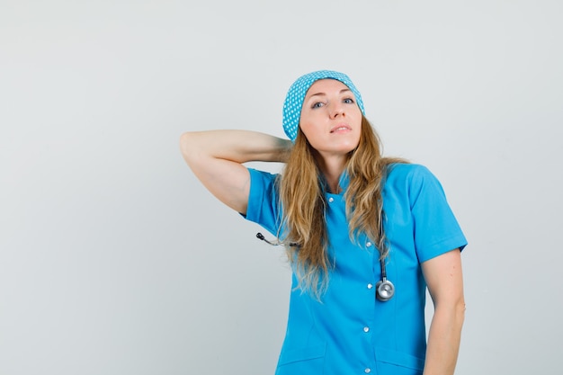 Female doctor posing with hand on neck in blue uniform and looking confident. 