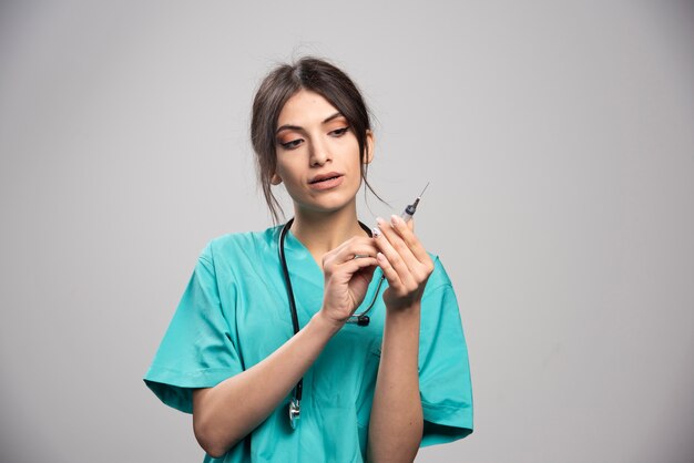 Female doctor posing with syringe on gray