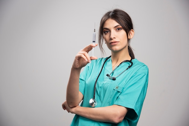 Female doctor posing with syringe on gray