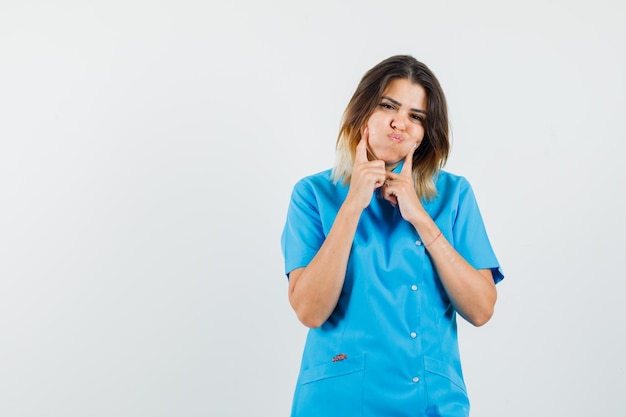 Женщина-врач нажимает пальцами на раздутые щеки в синей форме