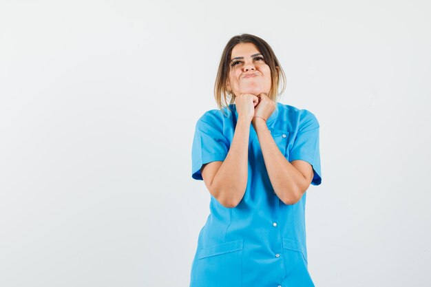 Female doctor propping chin on fists in blue uniform and looking hopeful