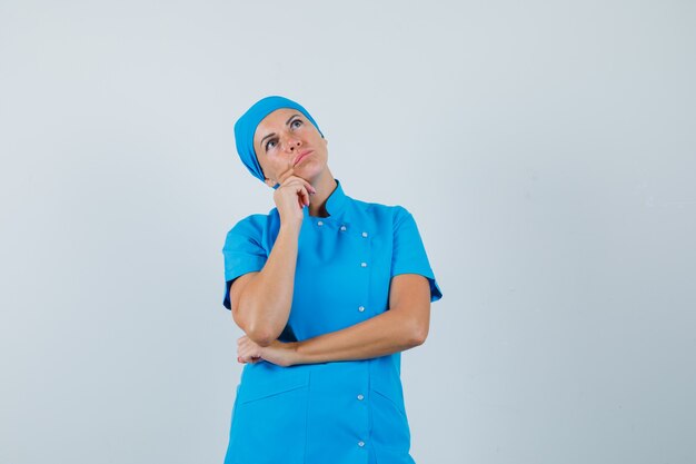 Female doctor propping chin on hand in blue uniform and looking pensive , front view.