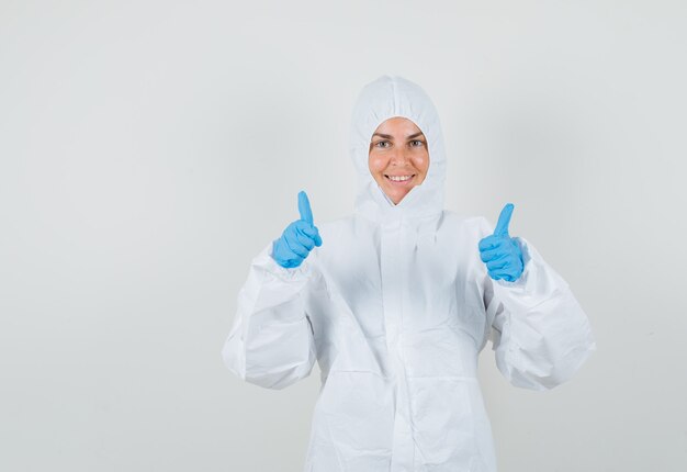 Женщина-врач в защитном костюме, перчатки показывает двойные пальцы вверх и выглядит счастливой
