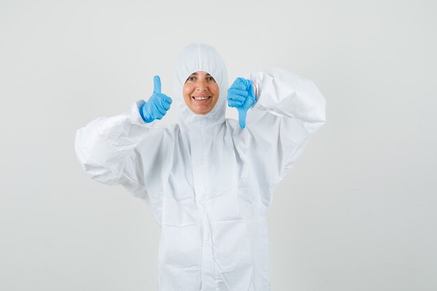 Free photo female doctor in protective suit, gloves showing thumbs up and down and looking glad