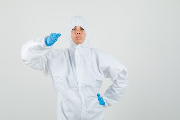 Female doctor in protective suit, gloves threatening with fist and looking strict