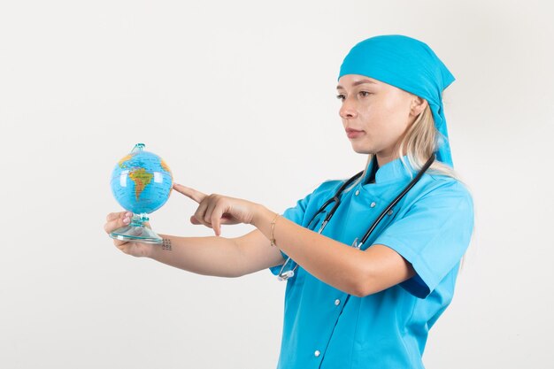 Female doctor putting finger on globe to choose destination in blue uniform .