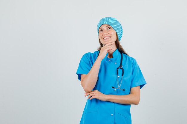 Female doctor putting hand while propping up on chin in blue uniform and looking cheerful. front view.